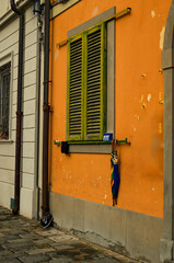 Vintage orange wall with window closed by green wooden shutters. Wall with rough surface. Wooden shutters on the window of a traditional house in Pisa. Typical architecture of Tuscany region, Italy