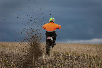 motocross dirtbike rider wheelie in field in front of dark blue sky  - obrazy, fototapety, plakaty