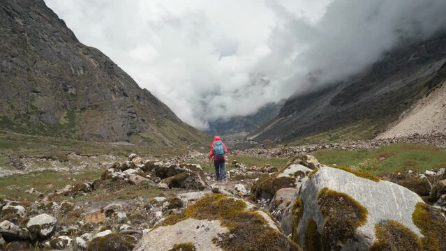 Lonely woman backpacker trekker dressed bright jacket going by mountain valley path on the Mera peak climbing route near Tagnag settlement at cca 4150m. Active people wide mountain valley 4K video.