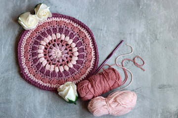 Crocheted trivet made of pink organic yarn. Handmade crochet potholder on gray background with...