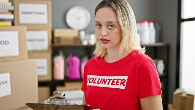 Young blonde woman volunteer writing on checklist smiling at charity center