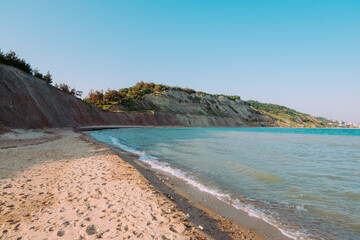 Peaceful Sandy Beach on the Aegean Sea with Gentle Waves, Rocky Hills, and Clear Blue Sky on a Bright Summer Day