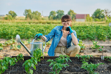 Woman with watering can, smiling female looking at camera at vegetable garden
