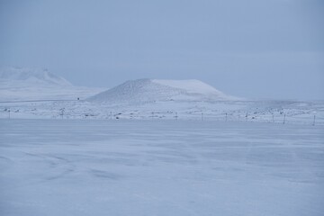 Hill in the distance and a fenced field completely covered with snow in winter