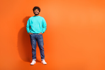 Full size photo of nice positive young man put hands pockets posing empty space isolated on orange color background