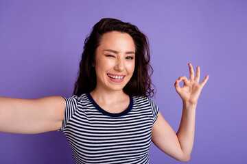Selfie photo of young pretty woman blinking eye show okey sign happy smiling making video blog isolated on violet color background