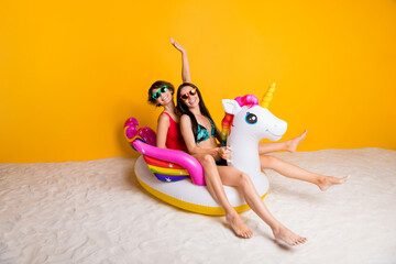 Photo of positive girls enjoy swim ride in unicorn rubber buoy on bay lagoon isolated shine color background © deagreez