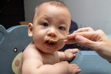 Beginning of complementary nutrition. 6 month old baby eating guava porridge. Child has fun with...