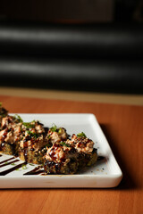 Hot roll, enrolado em uma nori, coberto por cebolinha e cream cheese, coberto com molho tarê, em um prato de cerâmica e wallpaper