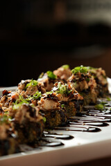 Hot roll, enrolado em uma nori, coberto por cebolinha e cream cheese, coberto com molho tarê, em um prato de cerâmica e wallpaper