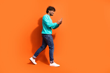 Side profile photo of young positive happy guy walking using smartphone texting girlfriend for a date isolated on orange color background