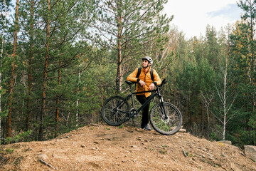 a sporty lifestyle.A man in a protective helmet and equipment stands next to a mountain bike and enjoys nature