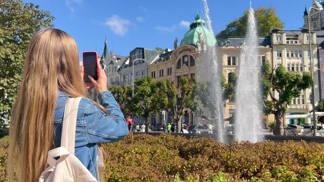Stylish woman traveler with a backpack walks and takes photos of a fountain in the Old Town in Europe