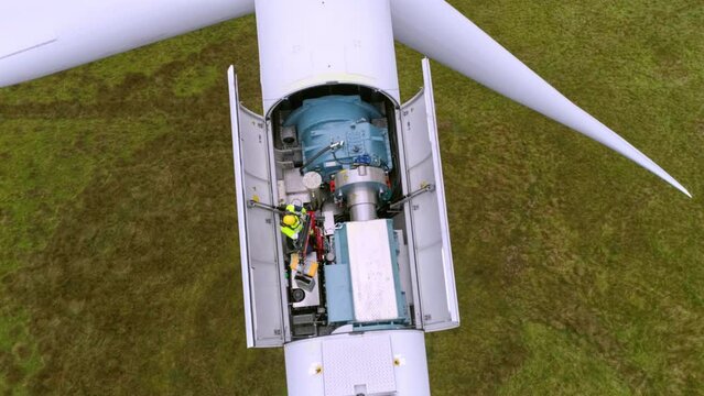 Anonymous man working on wind turbine. Aerial top down view of windmill farm for energy production on beautiful cloudy sky in highlands.