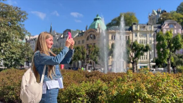 A woman takes photos with a smartphone of the beautiful tourist town of Karlovy Vary, Czech Republic