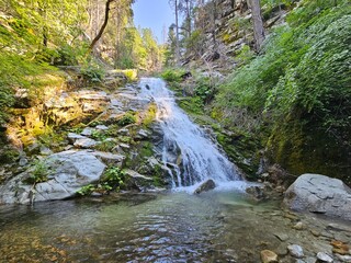 A beautiful waterfall deep in the California mountains cascading over mossy rocks into a clear creek bed surrounded by trees 