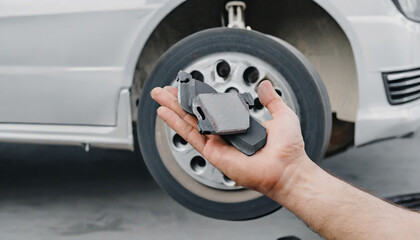 A man's hand with new brake pads on the background of a car without a wheel. Service work on replacing the front brake pads.