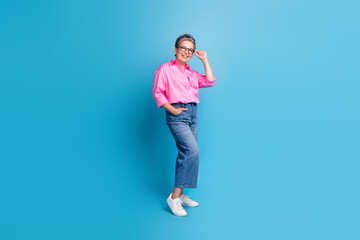 Full size photo of cheerful positive person wear stylish blouse jeans touching eyewear hand in pocket isolated on blue color background
