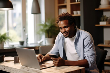 African American male entrepreneur talking over mobile phone and looking at camera while working over laptop at home