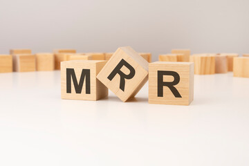 three wooden cubes with MRR symbols on them. white background. in the background there are many wooden blocks of different sizes