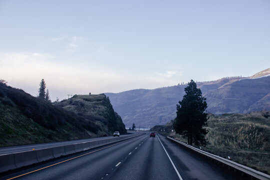 A highway surrounded by high mountains, along which cars drive with their headlights on at dusk