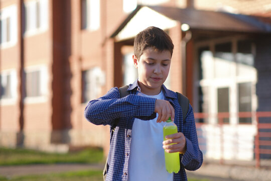 a cute fasion student boy of 12 years old open a plastic bottle of drink outdoor.