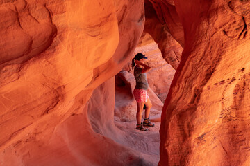 Woman standing in the fire cave and Windstone Arch in Valley of Fire State Park, Nevada, USA. Long, narrow slot canyon with sheer rock walls. Tranquil desert landscape of eroded sandstone formation