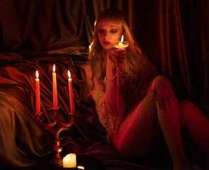 beautiful girl in a corset sits on the floor in the bedroom. admiring the dim candlelight. vintage...