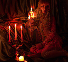 beautiful girl in a corset sits on the floor in the bedroom. admiring the dim candlelight. vintage...