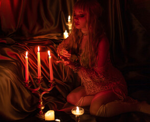 beautiful girl in a corset sits on the floor in the bedroom. admiring the dim candlelight. vintage...