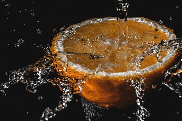 Fresh half-sliced orange fruit in water splashes isolated on black background