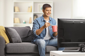 Young man watching tv and eating noodles