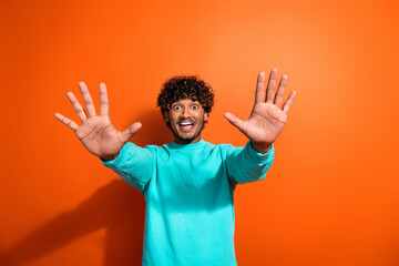 Portrait of funky youngster guy wearing trendy aquamarine sweatshirt raised palms ten amount sign isolated on orange color background