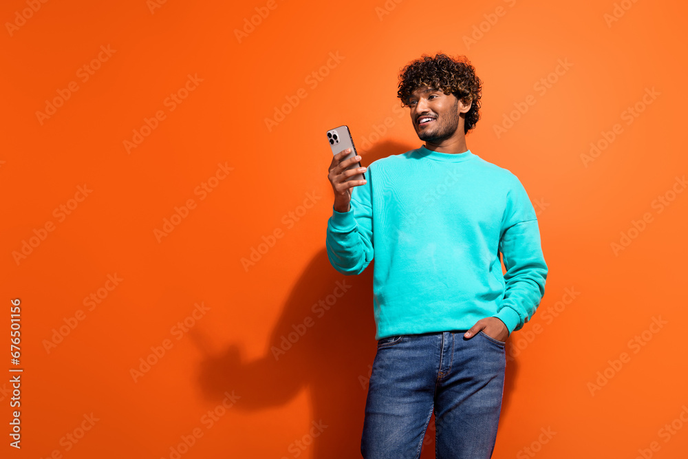 Wall mural Photo of attractive young arabian guy using his smartphone for online shopping with high discounts isolated on orange color background