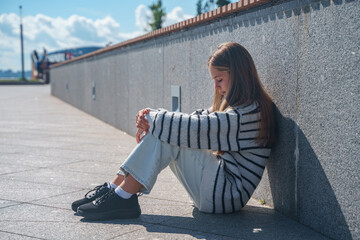 Sad teenage girl sitting alone on the asphalt in the city, teenage depression,the concept of...