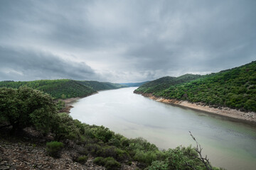 Landscape of a river surrounded by nature and green forest in autumn, a cloudy and rainy day.