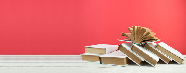 Open books, hardback colorful books on wooden table. Red background. Back to school. Copy space for...