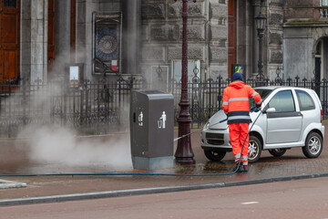 Employee of the cleaning service of the municipality of Amsterdam cleans the street with water. - obrazy, fototapety, plakaty