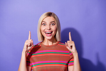 Photo of young shocked lady in striped t shirt amazed indicate fingers above head proposition discount isolated on violet color background