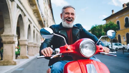 Cercles muraux Scooter Excited senior man riding red scooter in Italy, cheerful retired bearded hipster enjoying holiday, motorcycle road trip, trendy vacation lifestyle
