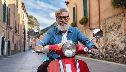 Selbstklebende Fototapeten Excited senior man riding red scooter in Italy, cheerful retired bearded hipster enjoying holiday, motorcycle road trip, trendy vacation lifestyle © Marko