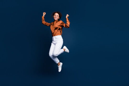 Full size photo of attractive young woman jumping win lucky wear trendy brown satin formalwear isolated on dark blue color background