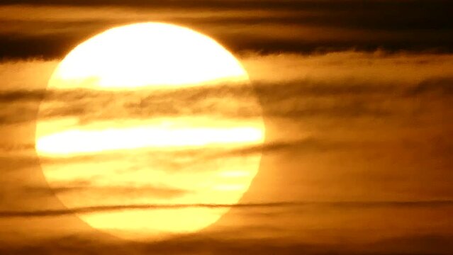 Dark red and orange sky with moving clouds and yellow sun disc during sunrise - real time. Topics: sun energy, weather, space, atmosphere, dawn