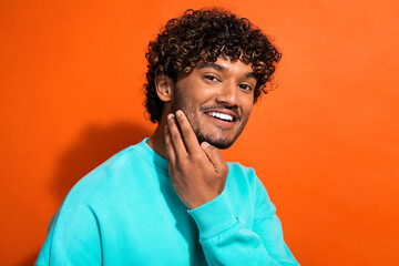 Photo of nice positive young man toothy smile arm touch beard chin isolated on orange color background - Powered by Adobe