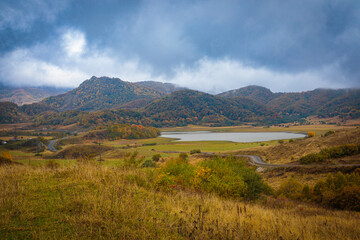Fototapeta premium Thick clouds slide down from the mountains and are swirled by the wind. Autumn landscape in the mountains near the lake.