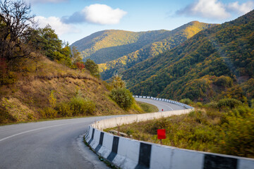 Winding road to the mountains. Sunny autumn in the mountains covered with bright colorful trees.