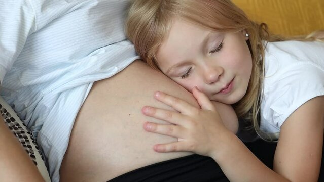 Little girl put her ear to her pregnant mother's belly.