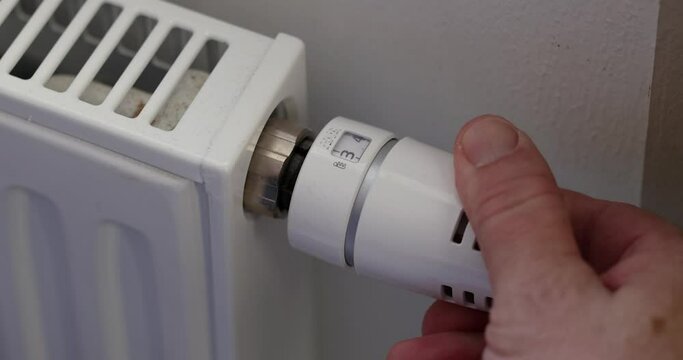 Heat radiator knob Hand adjusting temperature on heating radiator. Energy efficiency in domestic heating by reducing the power of radiators with thermostatic valves. Savings in natural gas consumption