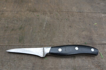 A small old kitchen knife with a black handle lies on an old wooden table