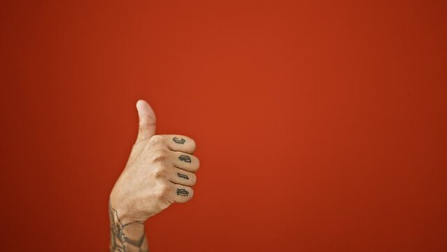 Man's tattooed hands thrust a credit card over isolated red background with an a-okay gesture - thumbs up in approval
